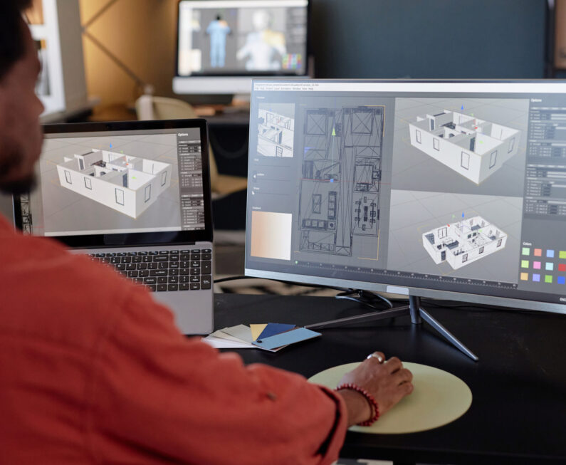 Person analyzing architectural designs on computer screens at office workspace, focusing on detailed models and layouts for a project. Engaging in work through high-end technology